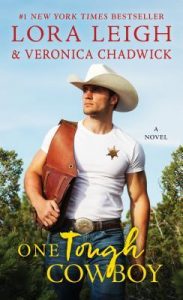 Hot cowboy walking through a leafy field wearing jeans and a white t-shirt and white stetson, carrying saddlebags over one shoulder and with a sheriff's badge on his tee.